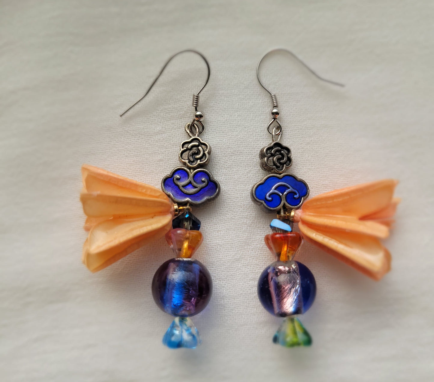Pair of earrings with blue beads and peach coloured flower decoration on a white background