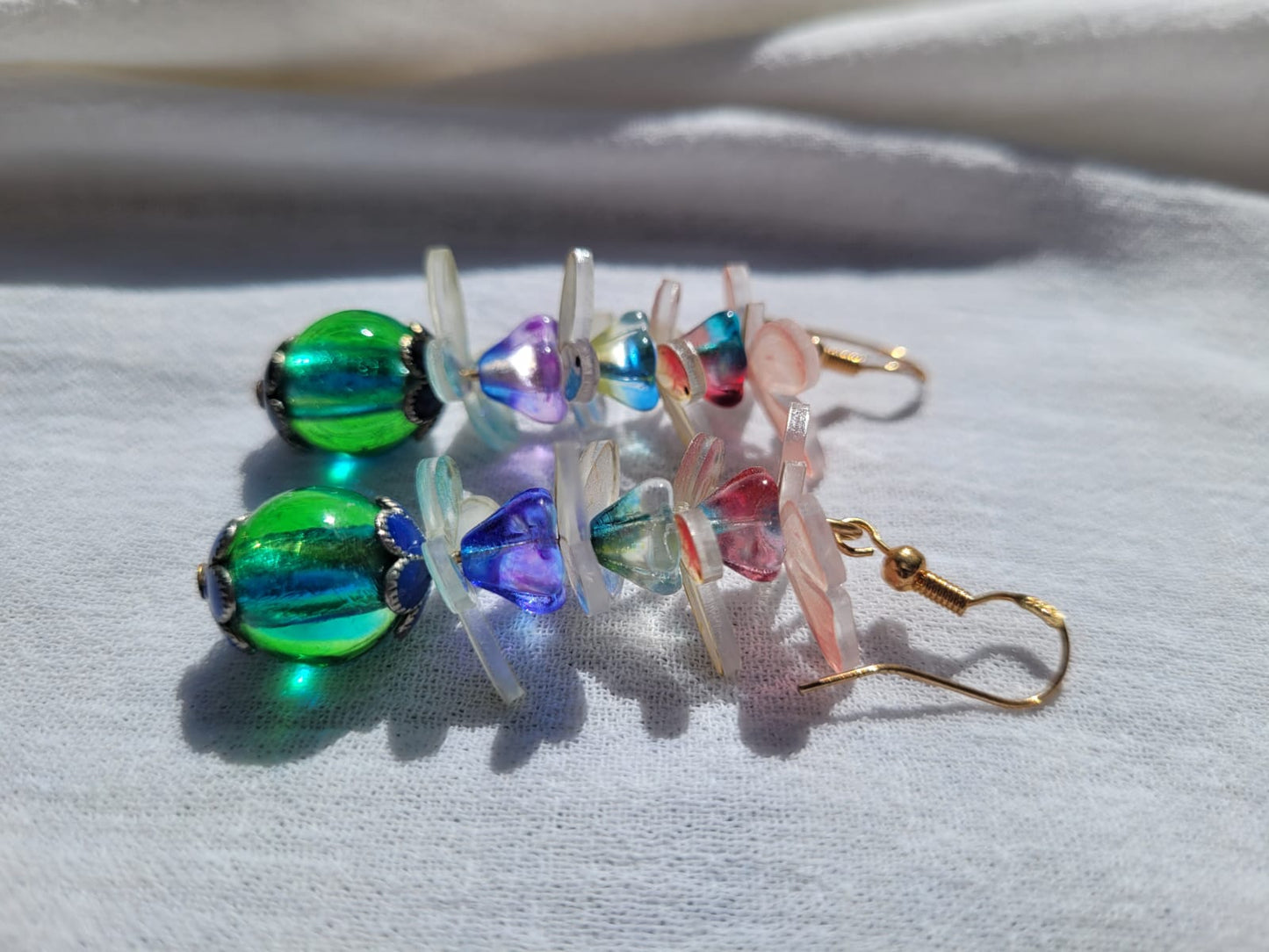 Colorful glass beads earrings with pale pink and white butterflies and gold plated hooks on a light gray background