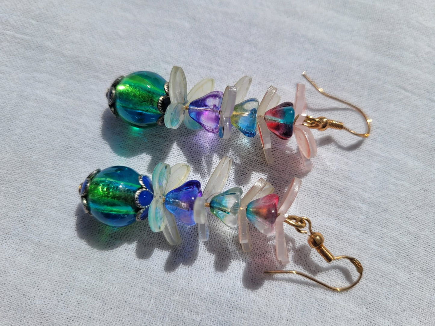 Colorful beaded earrings with pale pink and white butterflies and gold plated hooks on a light gray background