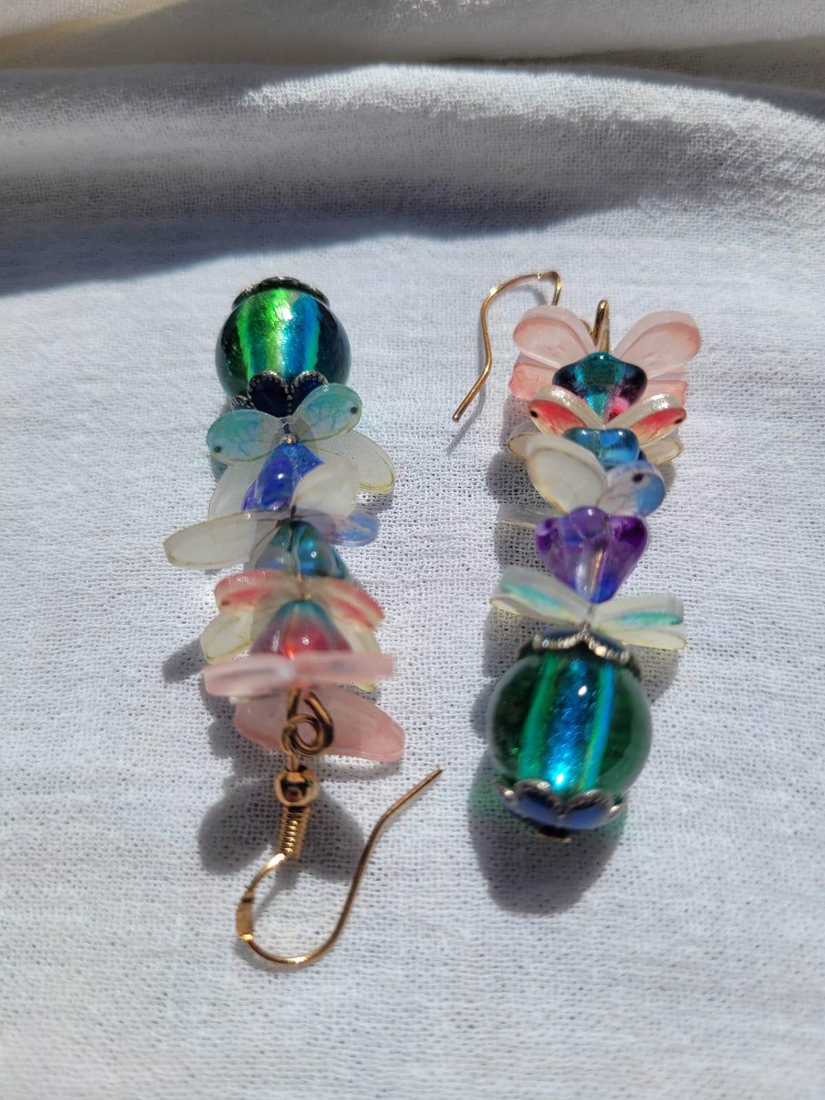 Colorful beaded earrings with pale pink and white butterflies and gold plated hooks on a light gray background