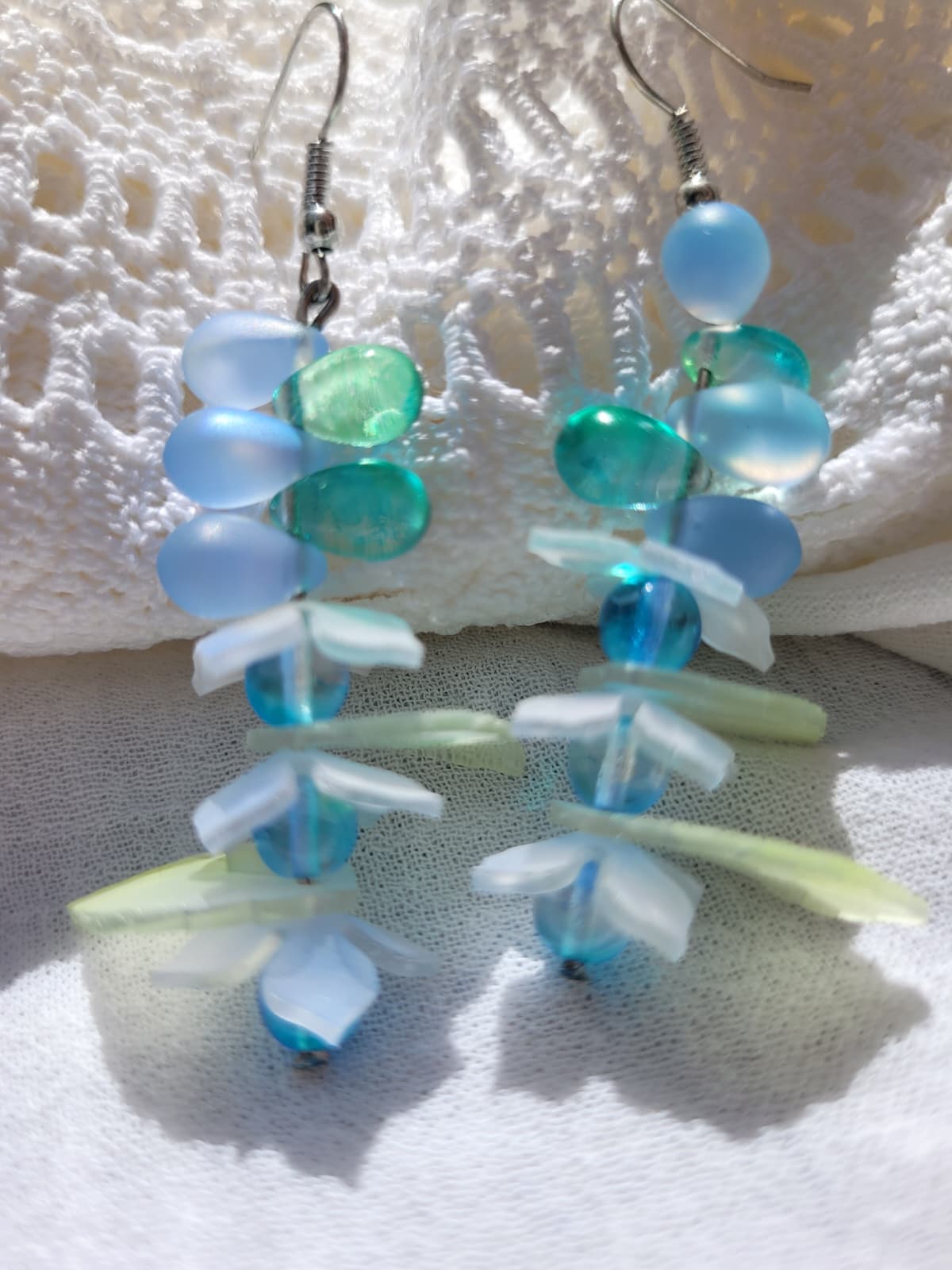 Pair of earrings with blue and green glass beads, acrylic leaves and small flowers on a white fabric background