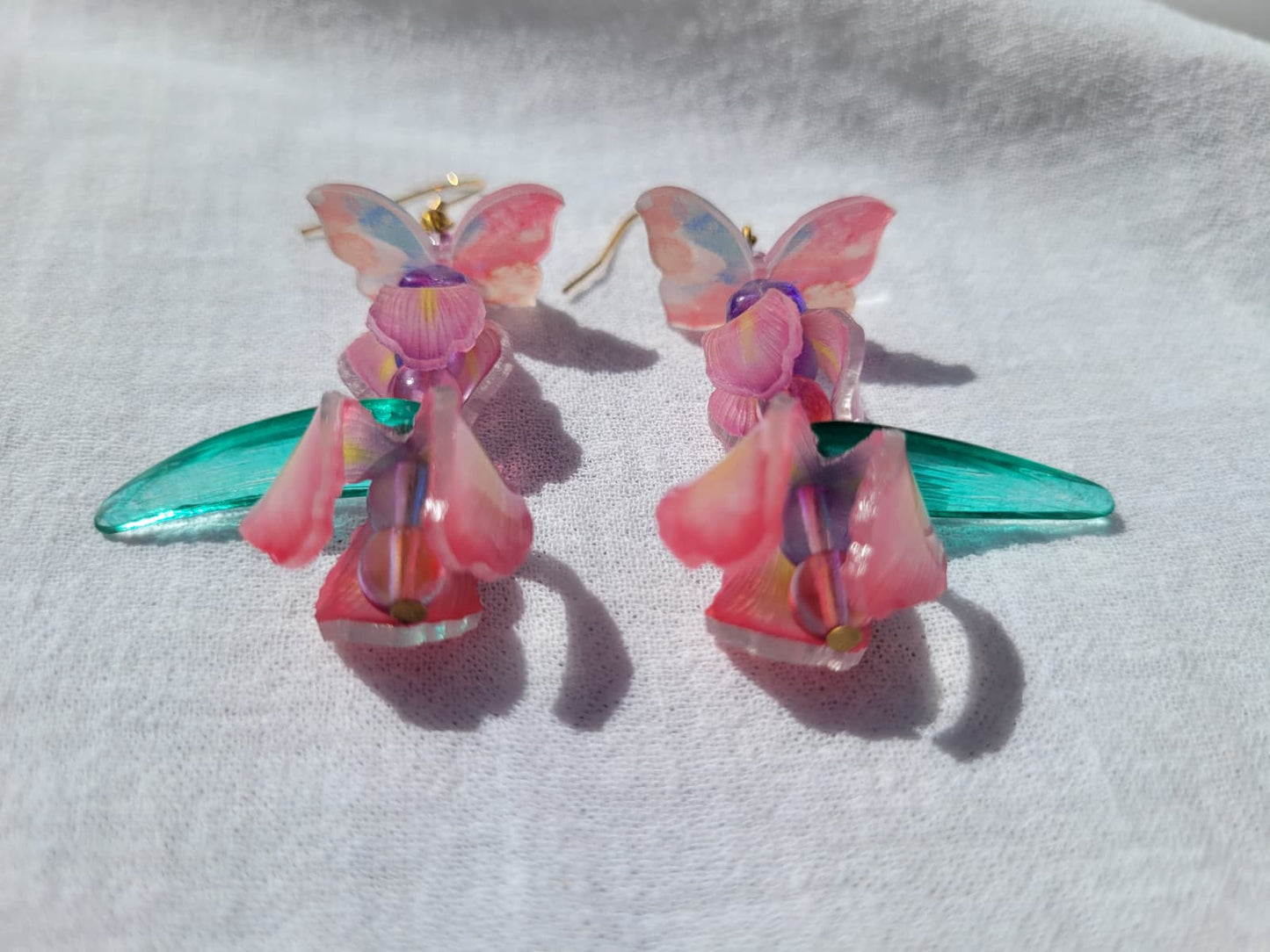 Pink iris-shaped earrings with green leaves and pink butterflies on a light gray fabric background