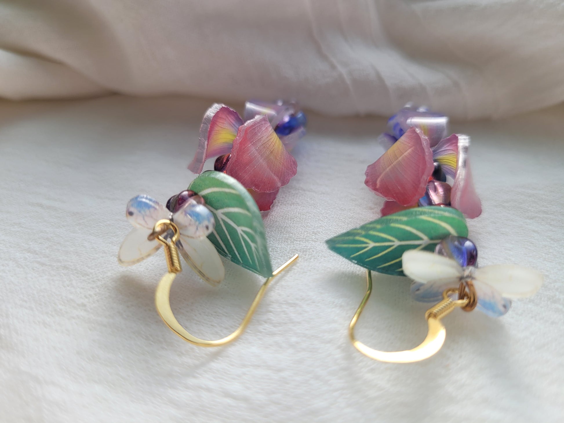Nature-inspired handmade iris and butterfly earrings with delicate gold-tone hooks on a white background.