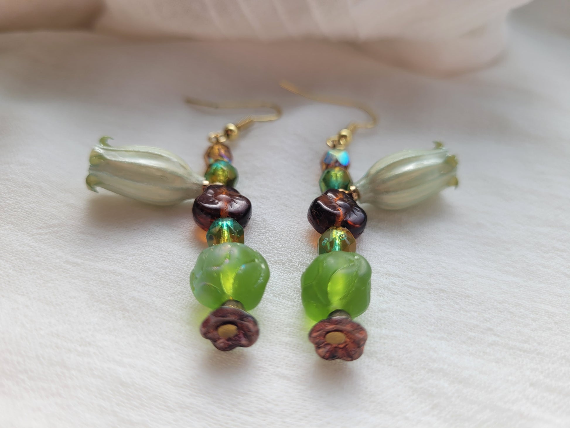 Beaded earrings with natural flowers, green, brown, and gold beads on a white background.