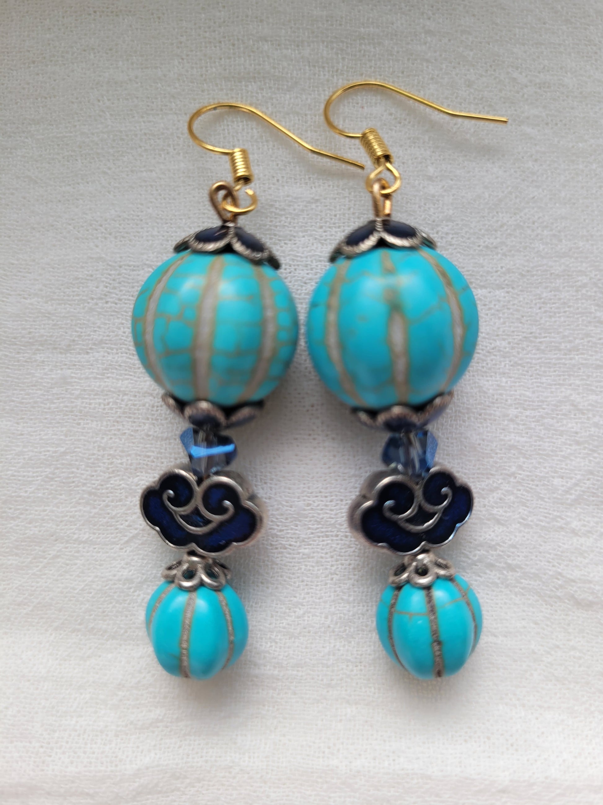 Turquoise beaded earrings with gold and silver accents on a light gray background