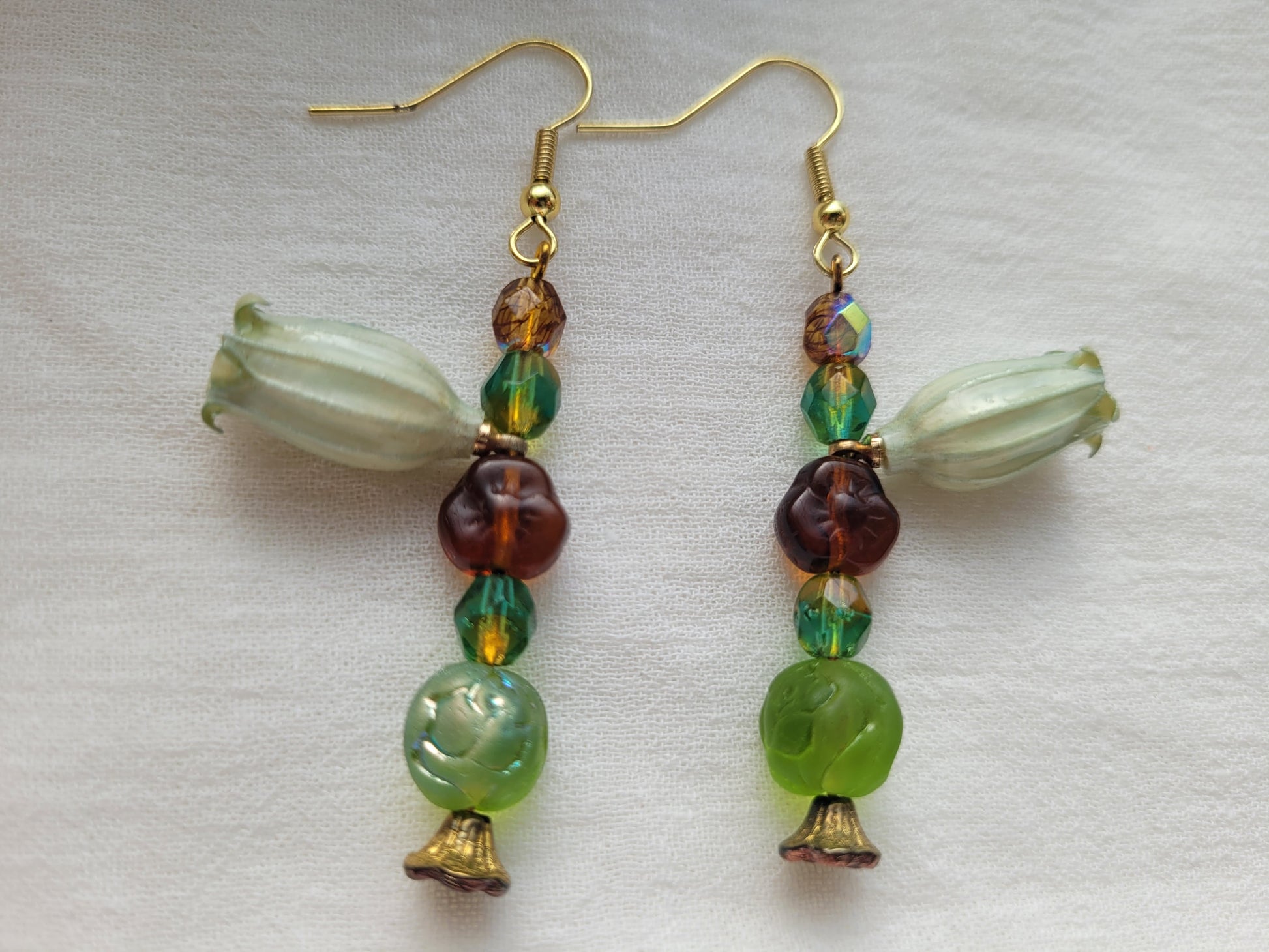 Beaded earrings with natural flowers, green, brown, and gold beads on a white background.