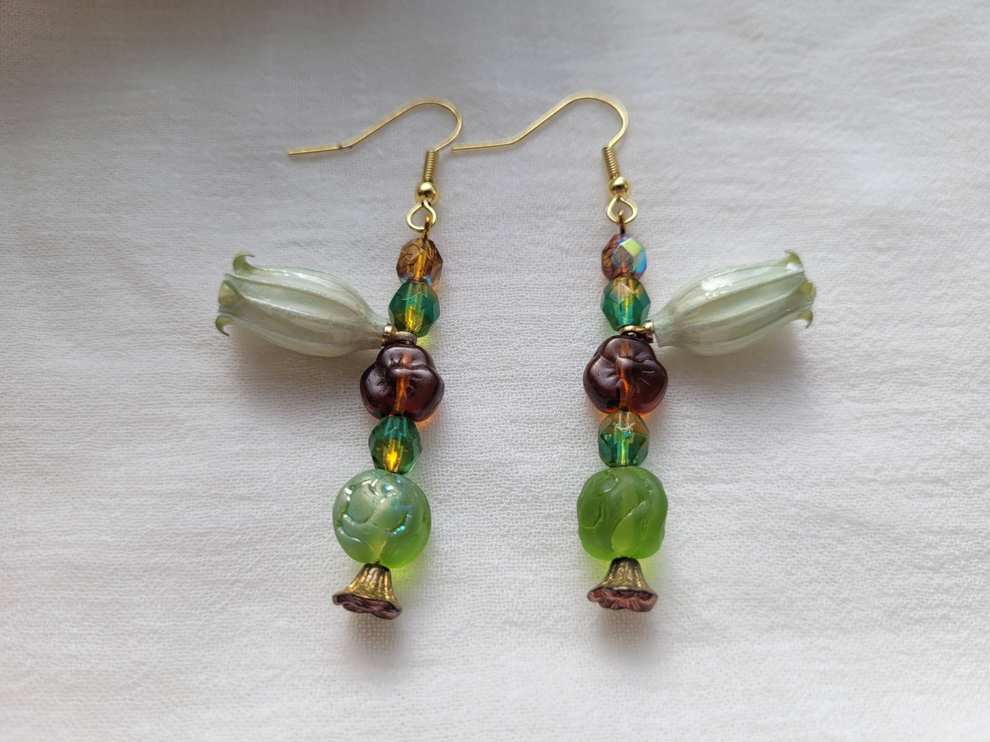 Beaded earrings with natural flowers, green, brown, and gold beads on a white background.