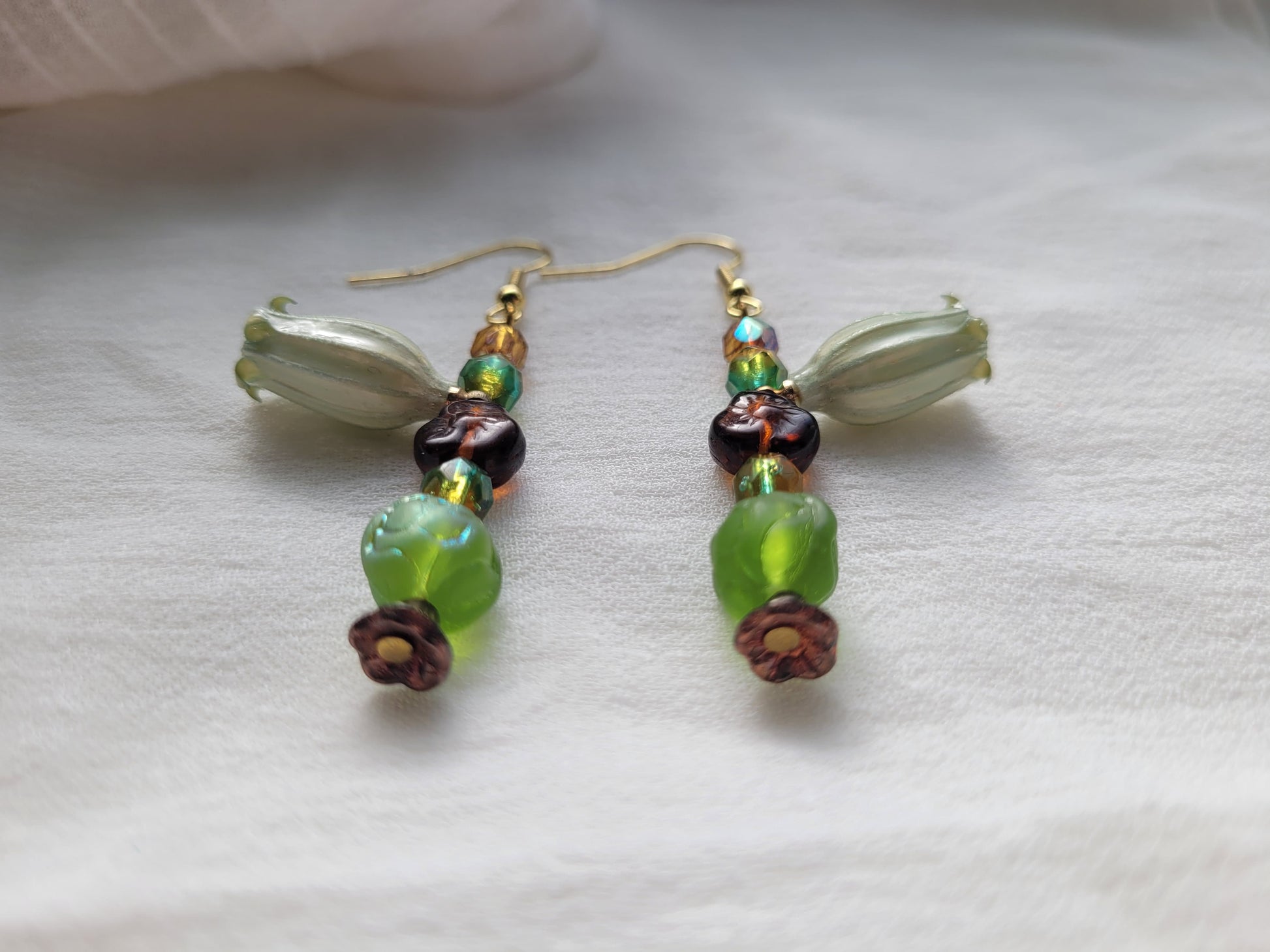 Beaded earrings with natural flowers, green, brown, and gold beads on a white background.
