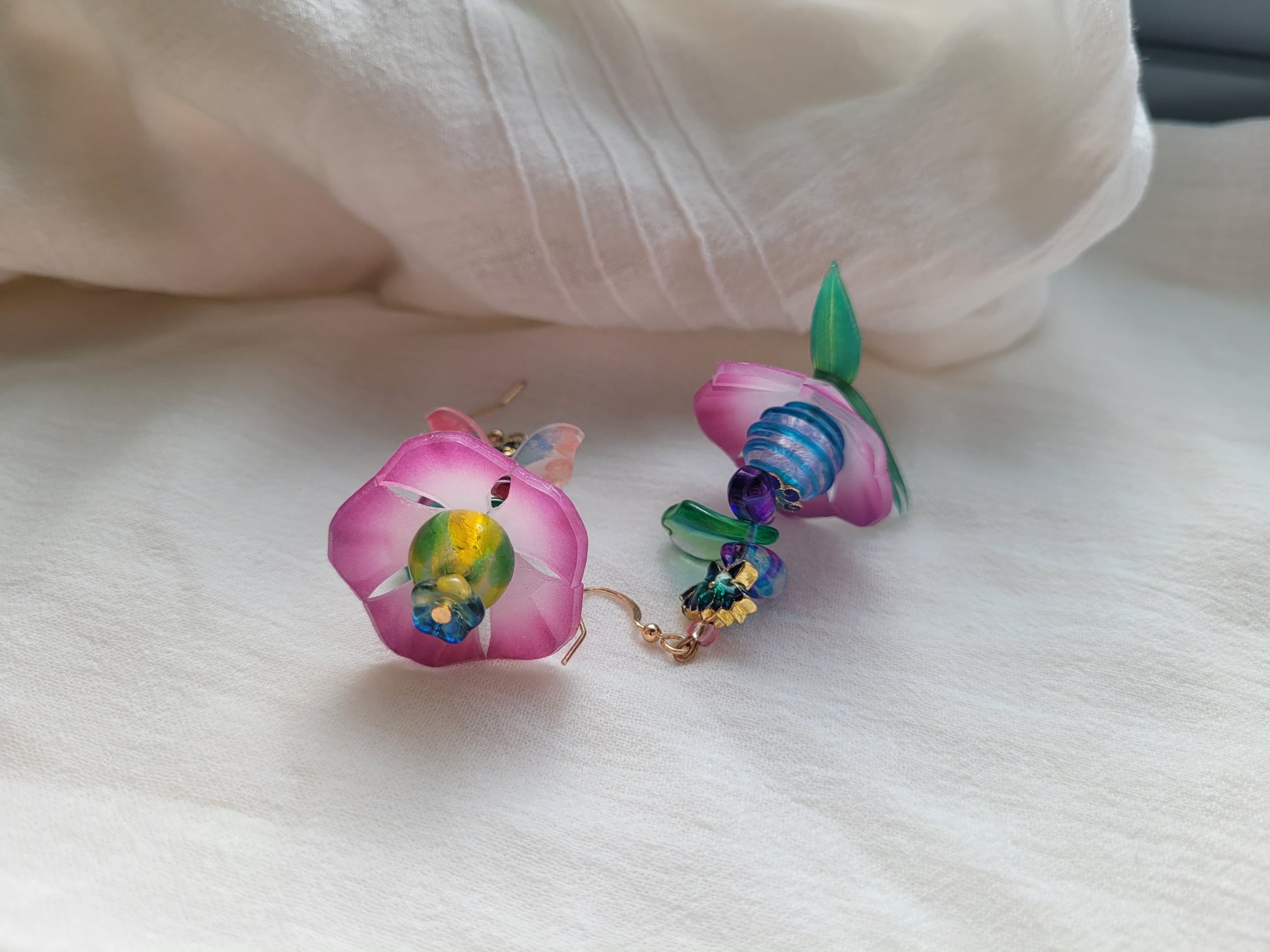 Colorful flower-shaped earrings on a white fabric background