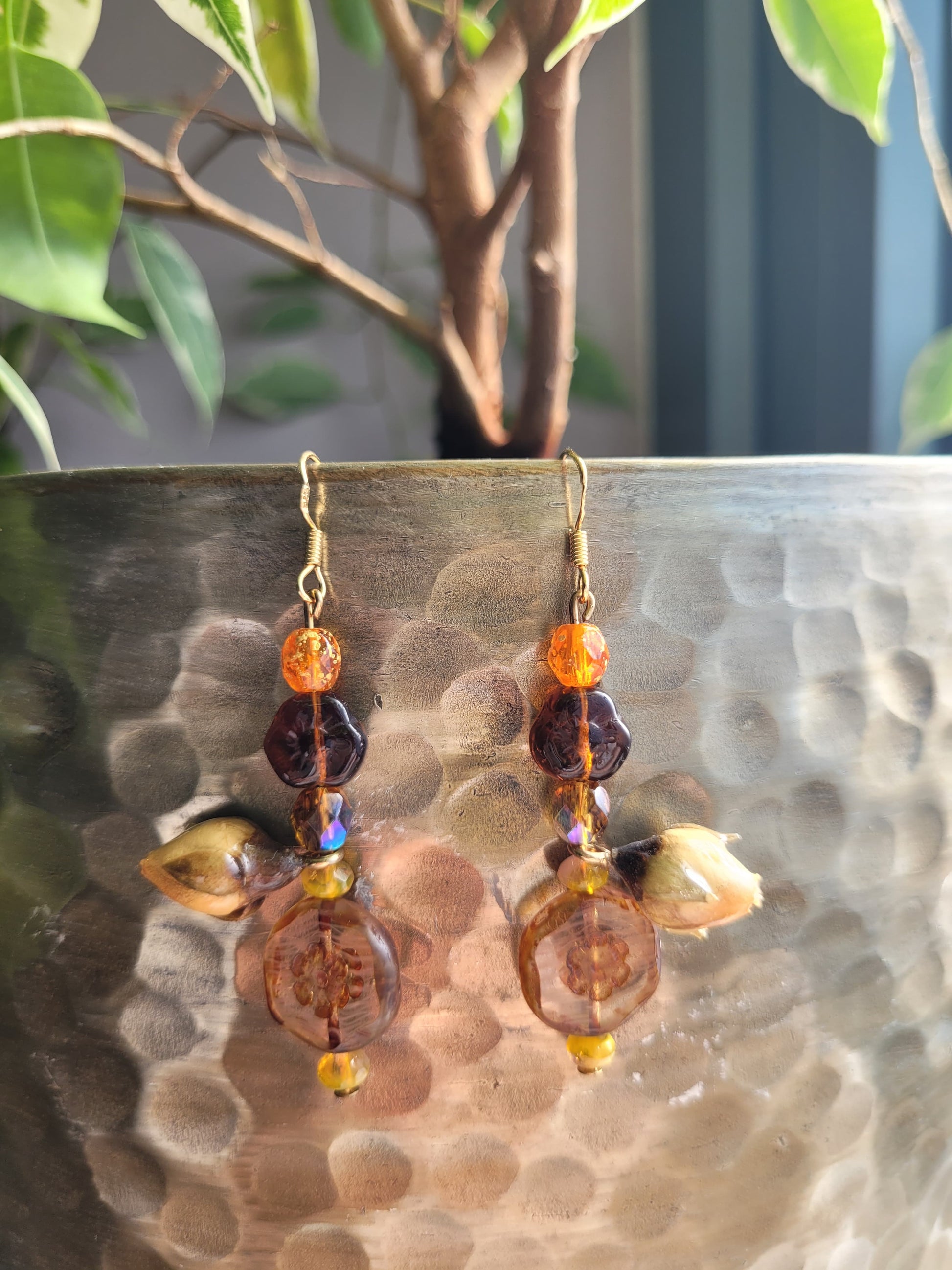 Pair of earrings with orange and purple beads on a textured surface with a plant in the background