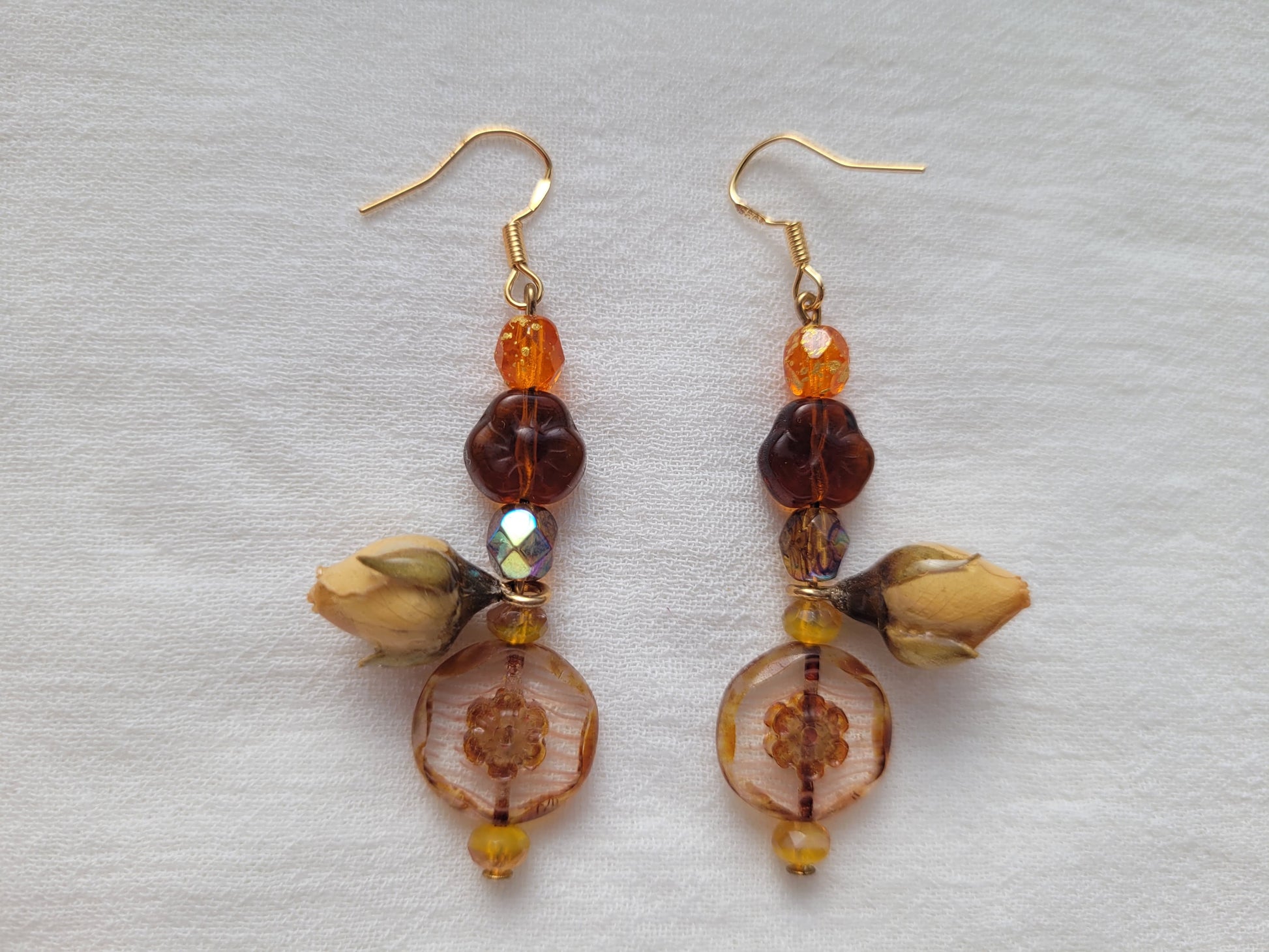 Pair of amber-colored beaded earrings with natural rose buds on a light gray background