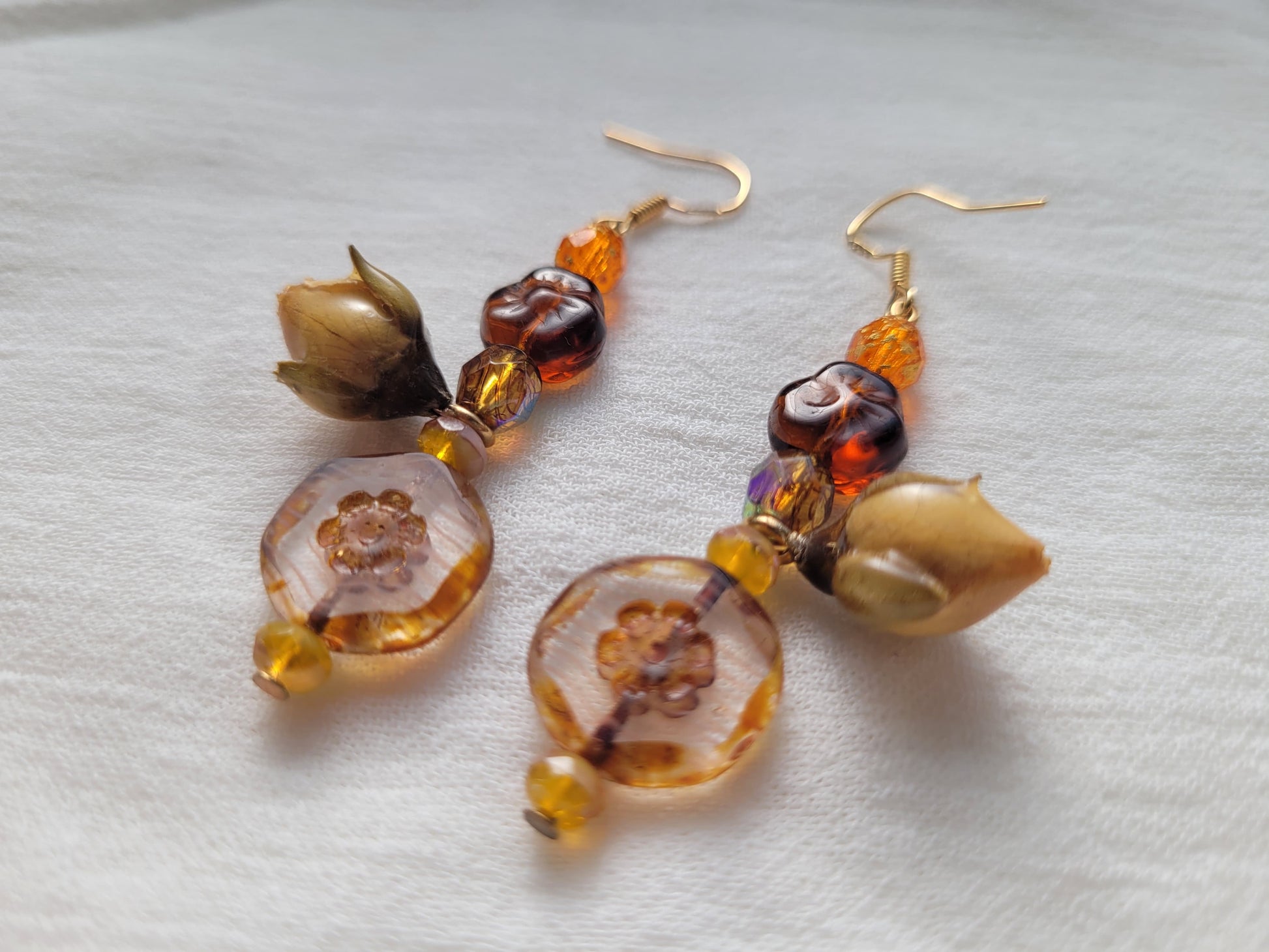 Pair of amber-colored beaded earrings with natural rose buds on a light gray background