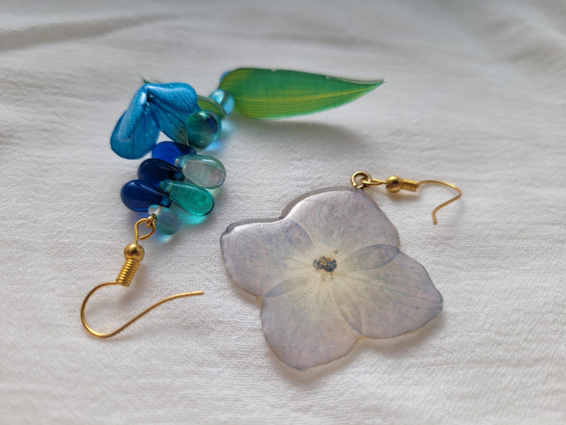 Pair of earrings with natural hydrangea flower and blue beads on a light gray background 