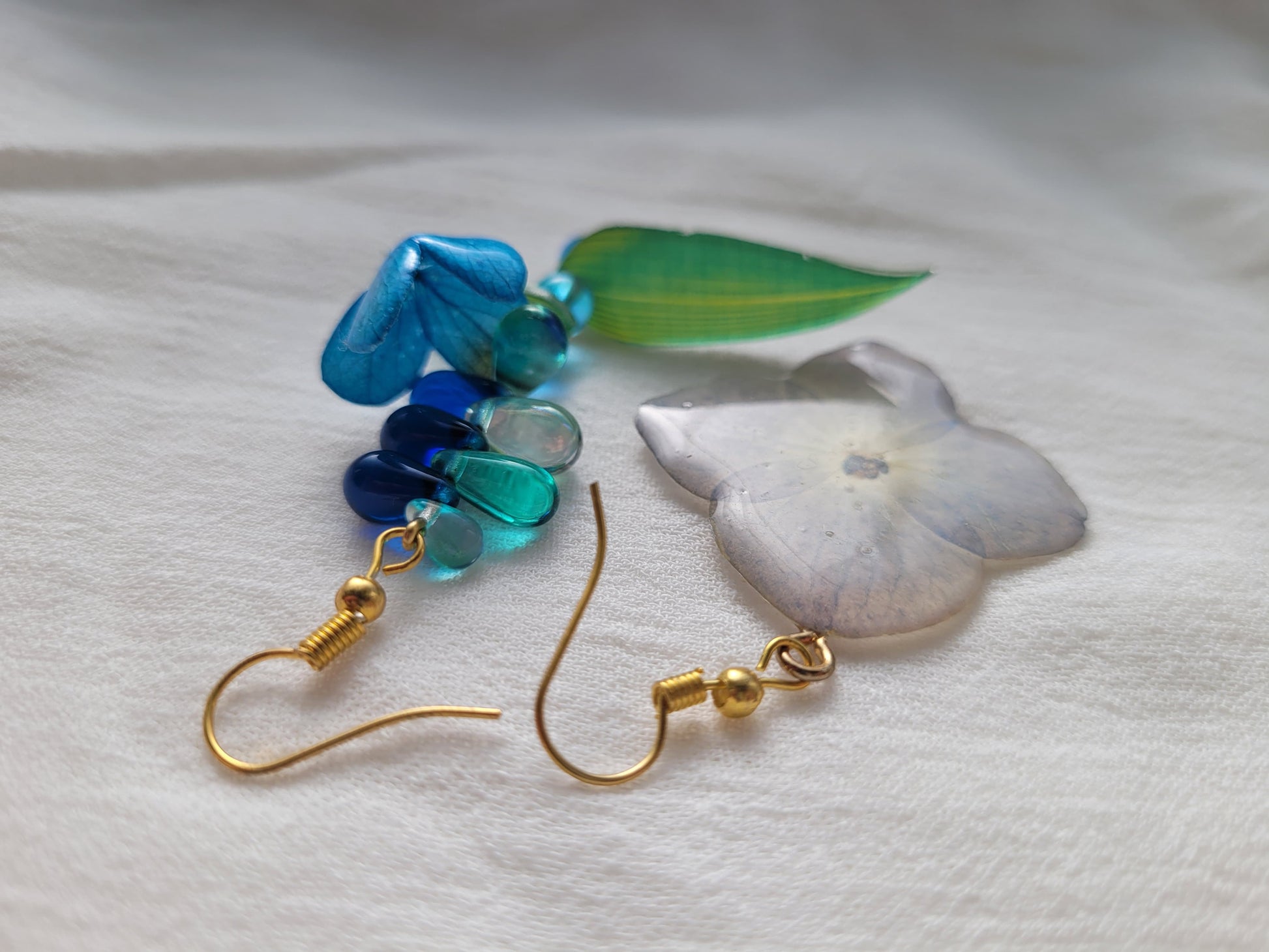 Pair of earrings with natural hydrangea flower and blue beads on a light gray background 