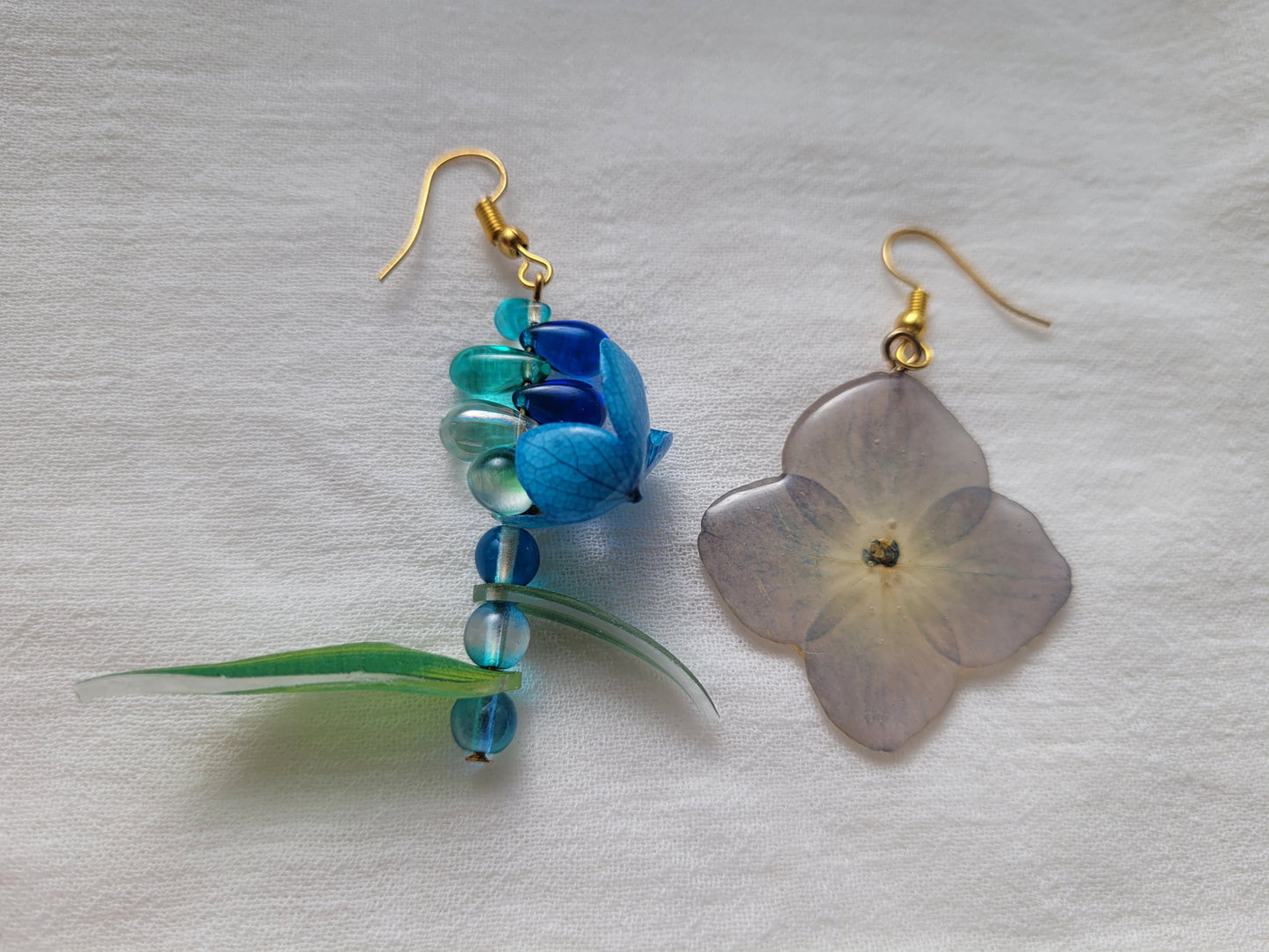 Pair of earrings with natural hydrangea flower and blue beads on a light gray background