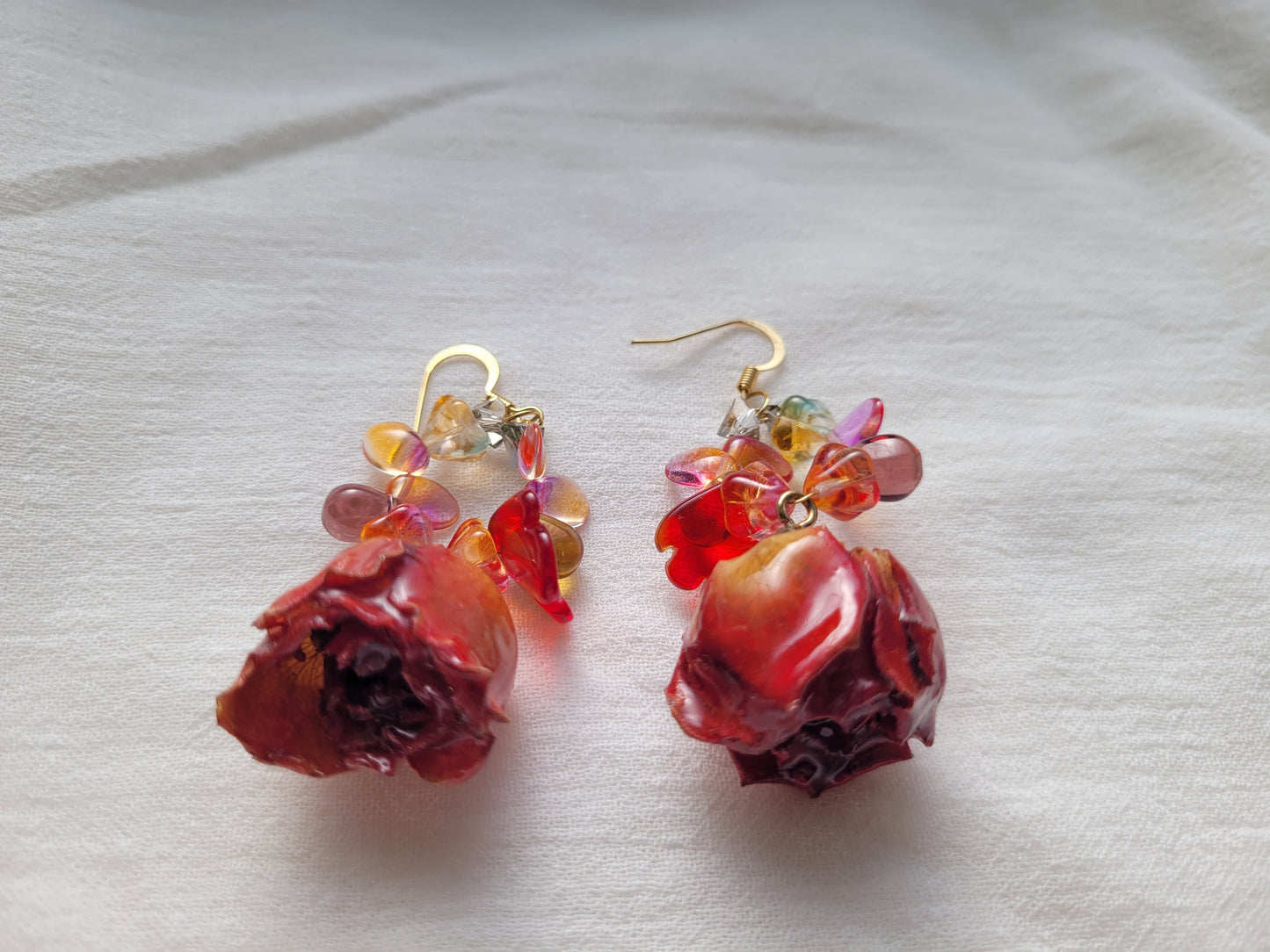 Pair of earrings with red roses and multicolored beads on a light background