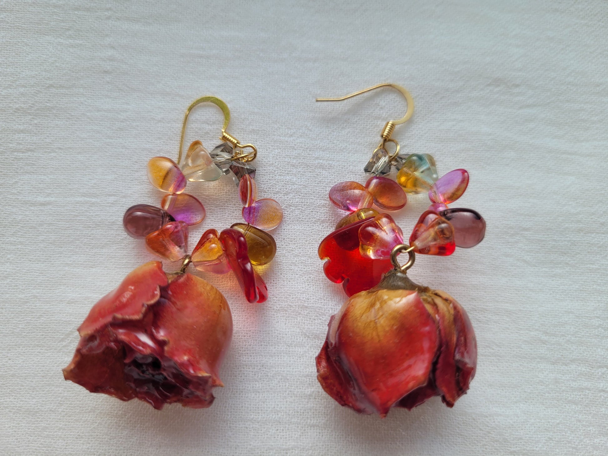 Pair of earrings with red roses and multicolored beads on a light background