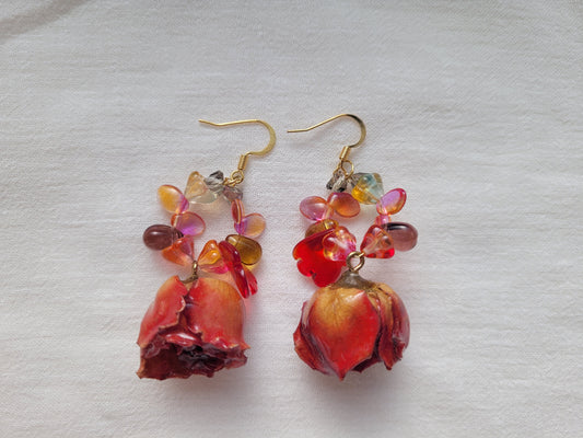 Pair of earrings with red roses and multicolored pastel beads on a light gray background