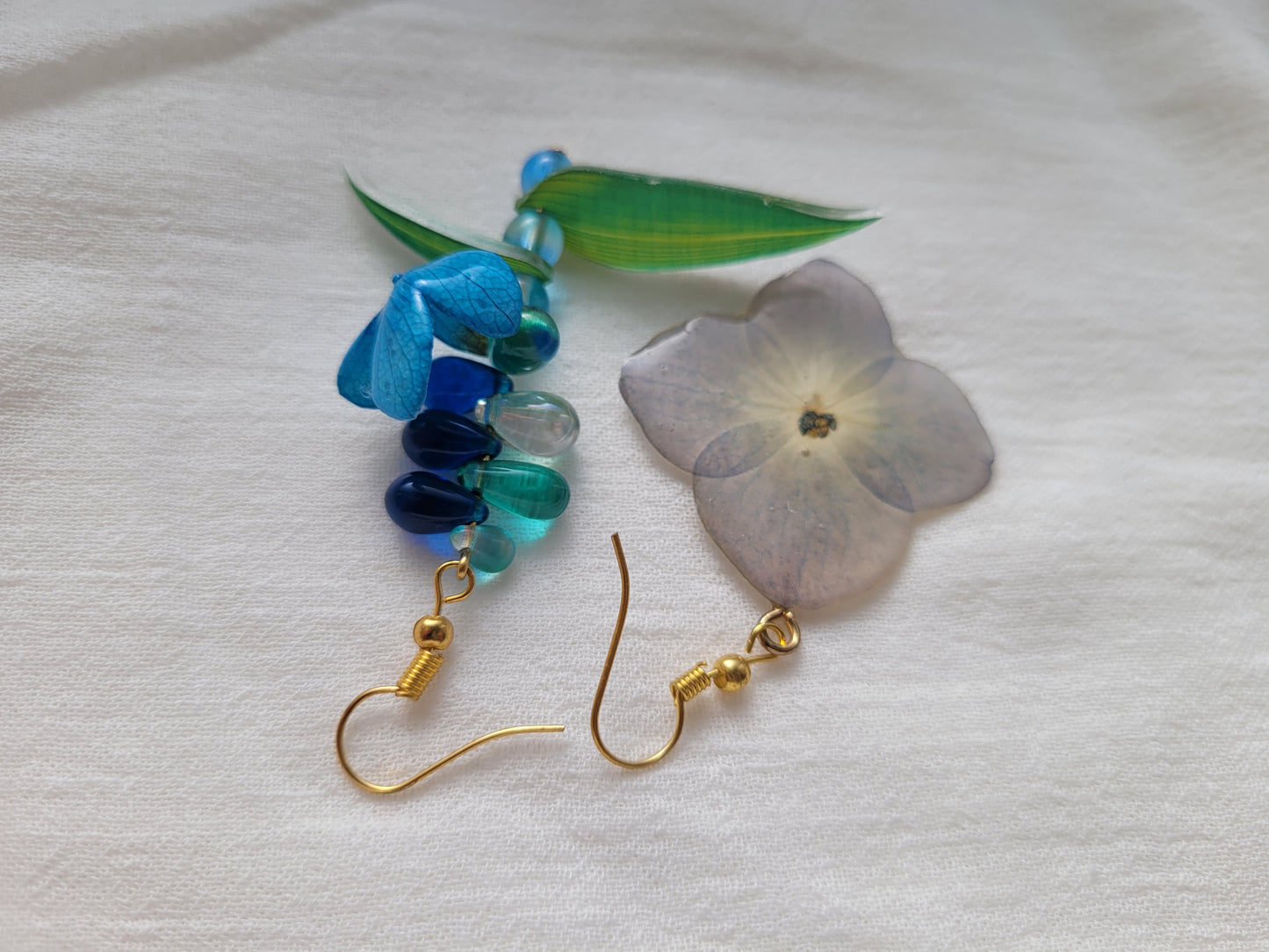 Pair of earrings with natural hydrangea flower and blue and green beads on a light gray background 