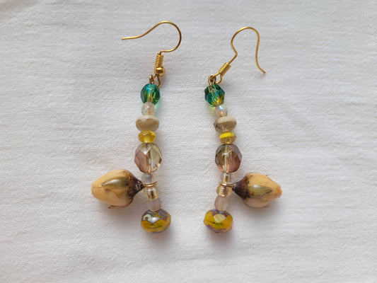 Pair of beaded earrings with natural yellow rose buds on a light fabric background