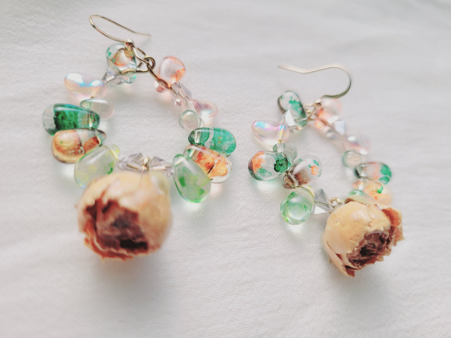 Pair of earrings with natural roses and bead details on a light background