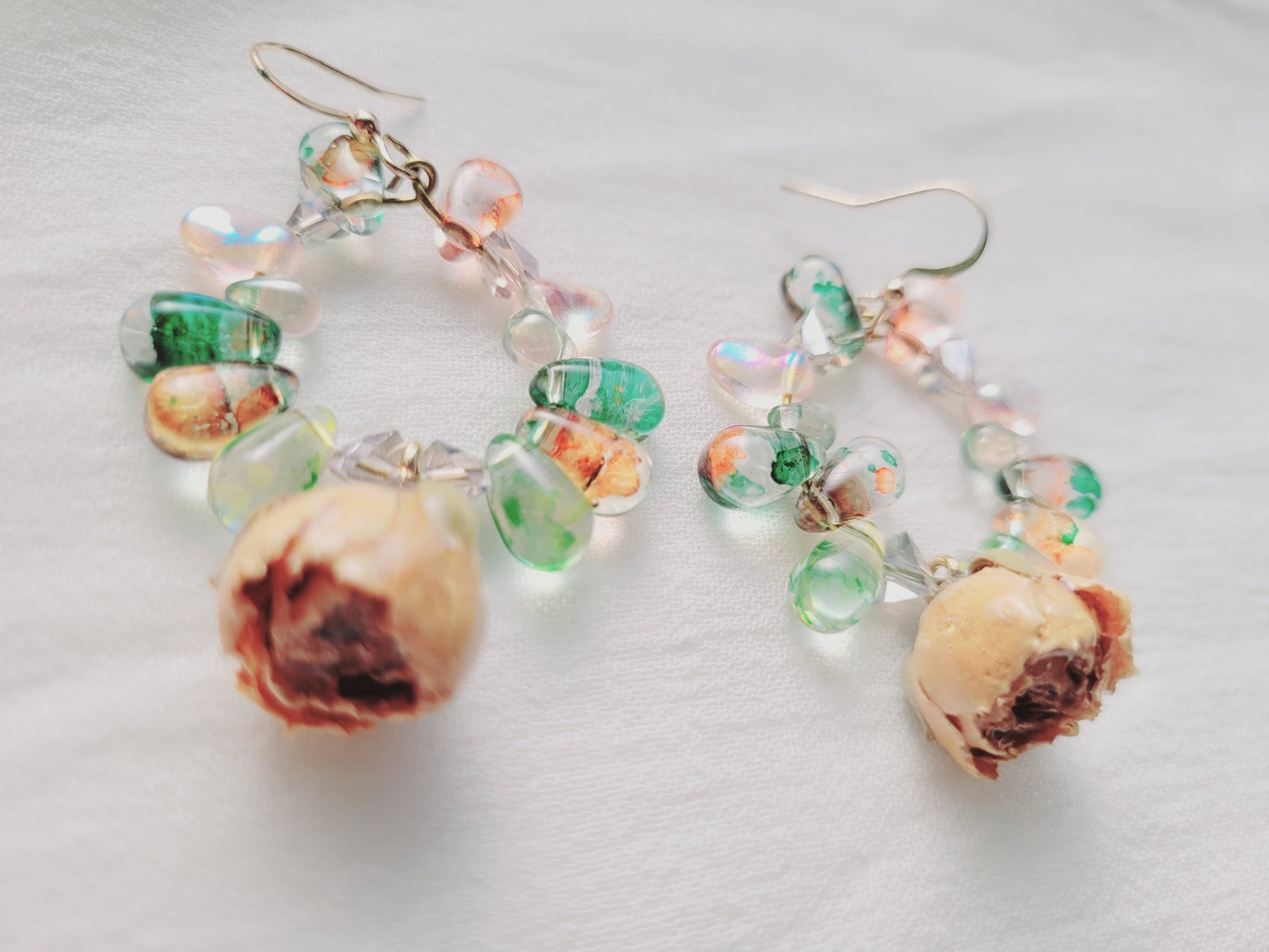 Pair of earrings with natural roses and bead details on a light background