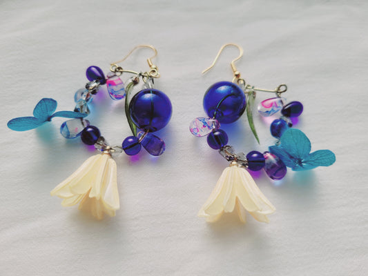 Pair of earrings with blue and purple beads and floral elements on a light gray background