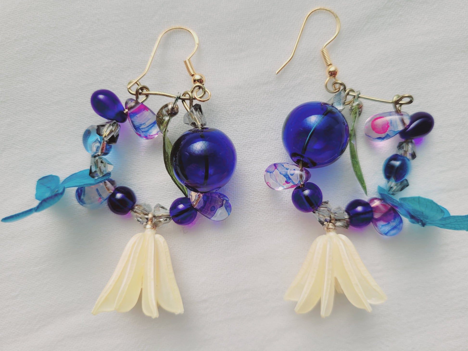 Pair of beaded earrings with blue and purple beads and yellow flower-like elements on a light gray background.