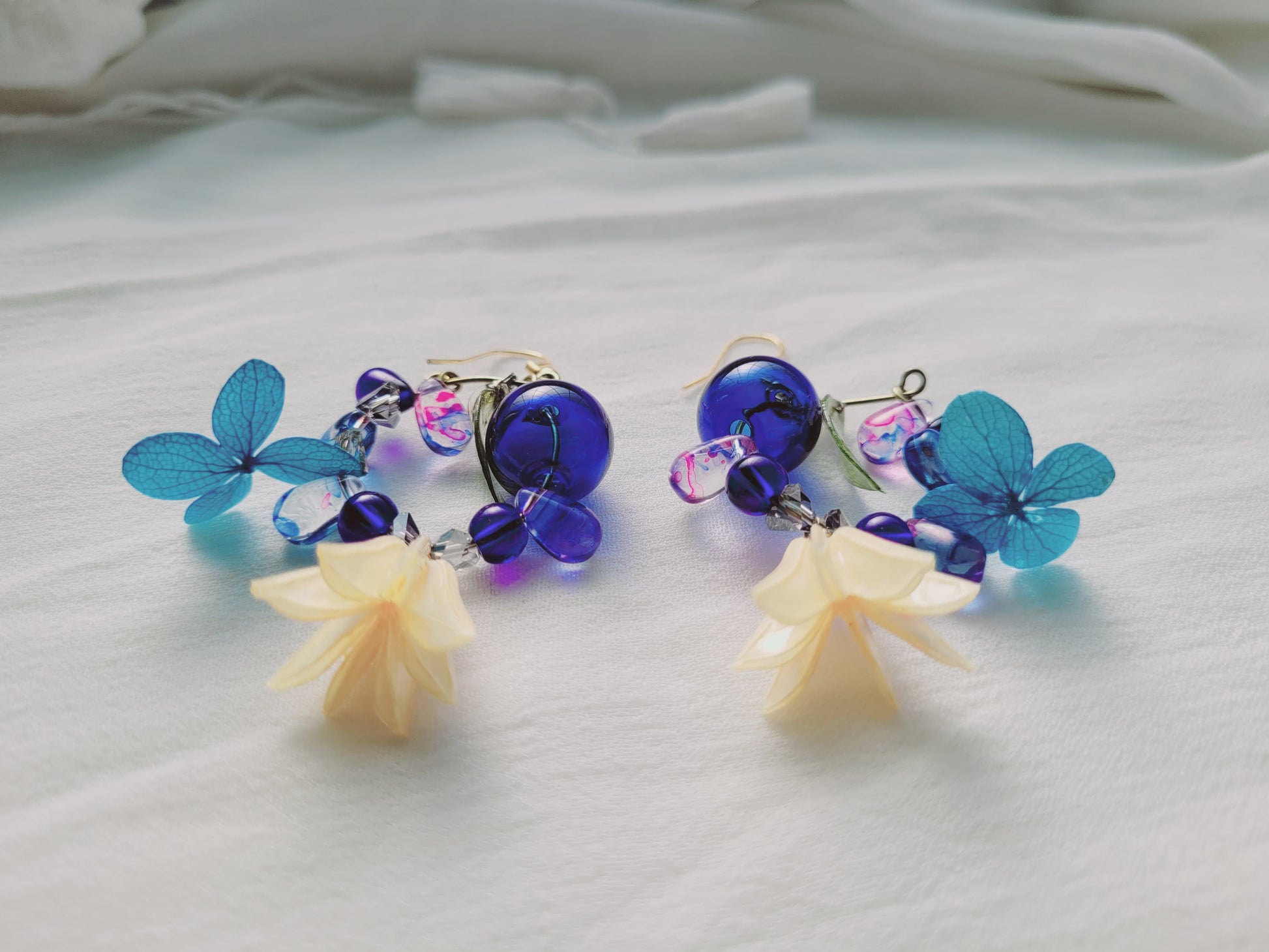 Pair of earrings with blue and purple floral designs on a white fabric background