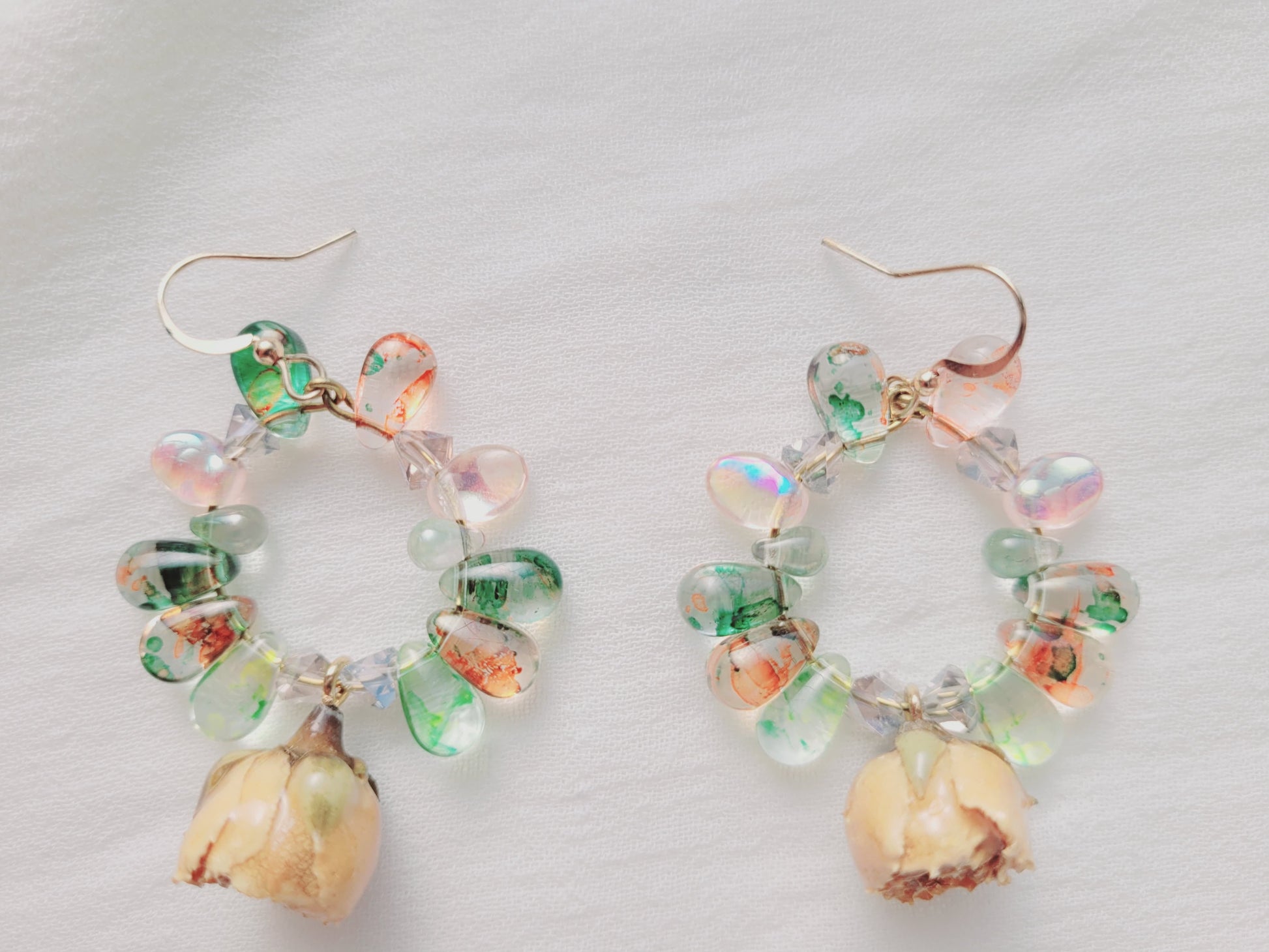Pair of earrings with colorful glass beads, natural yellow roses and shell-like charms on a light background