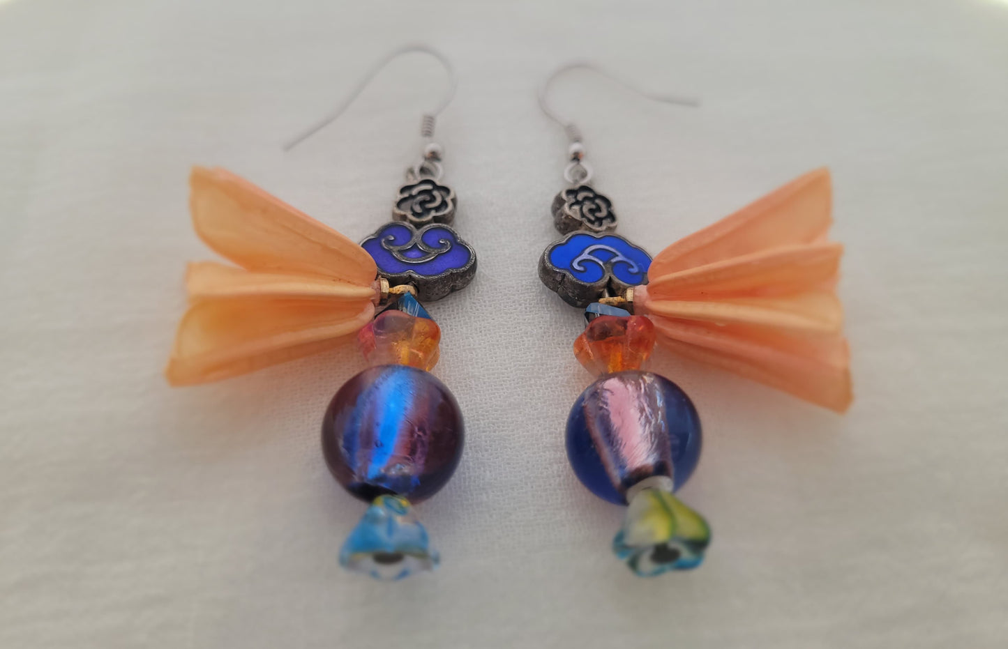 Pair of earrings with blue beads and peach coloured natural flower decoration on a white background