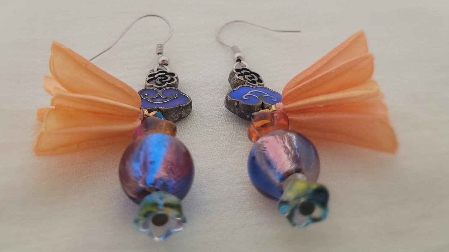 Pair of earrings with blue beads and peach coloured natural flower decoration on a white background