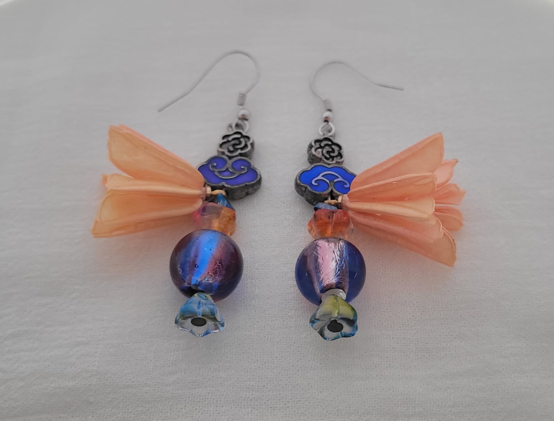 Pair of earrings with blue beads and peach coloured flower decoration on a light grey background