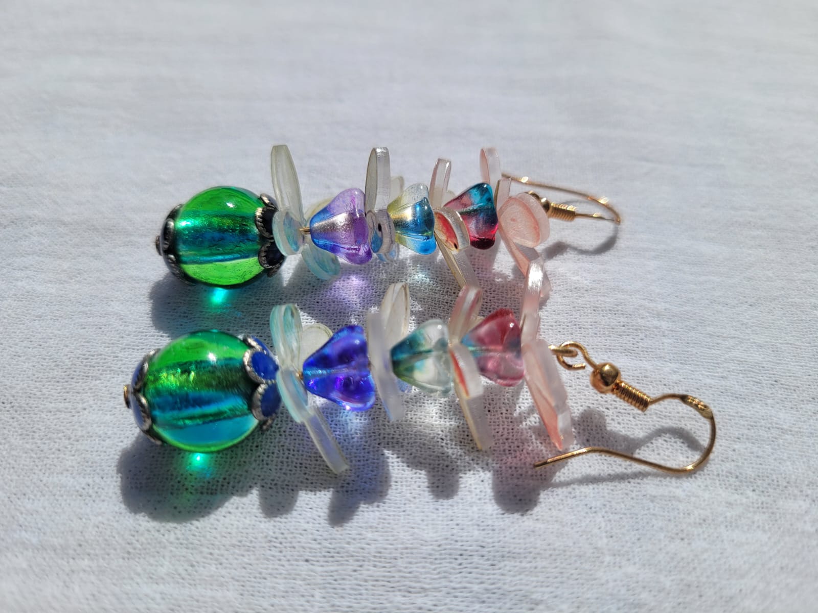 Colorful  glass beads earrings with pale pink and white butterflies and gold plated hooks on a light gray background 