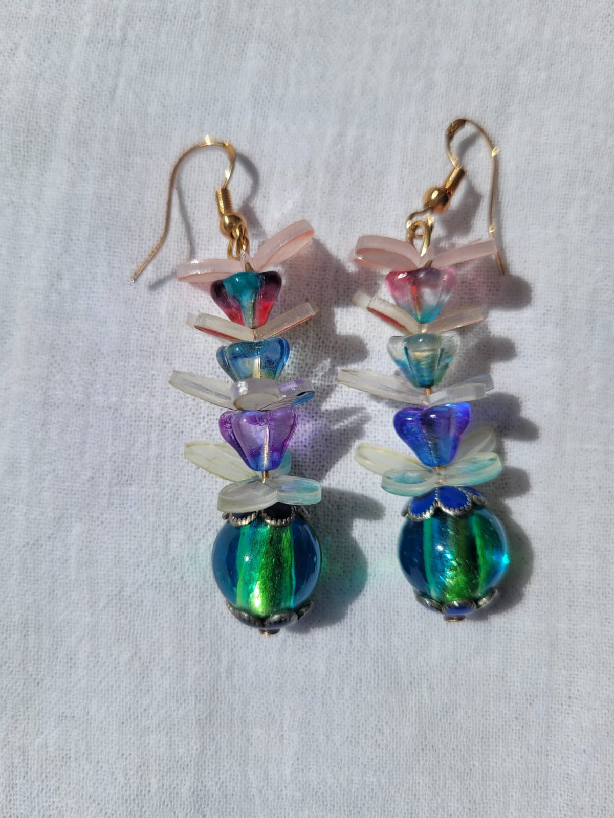 Colorful beaded earrings with pale pink and white butterflies and gold plated hooks on a light gray background 
