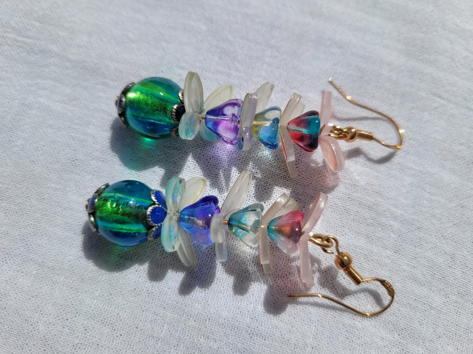 Colorful beaded earrings with pale pink and white butterflies and gold plated hooks on a light gray background 