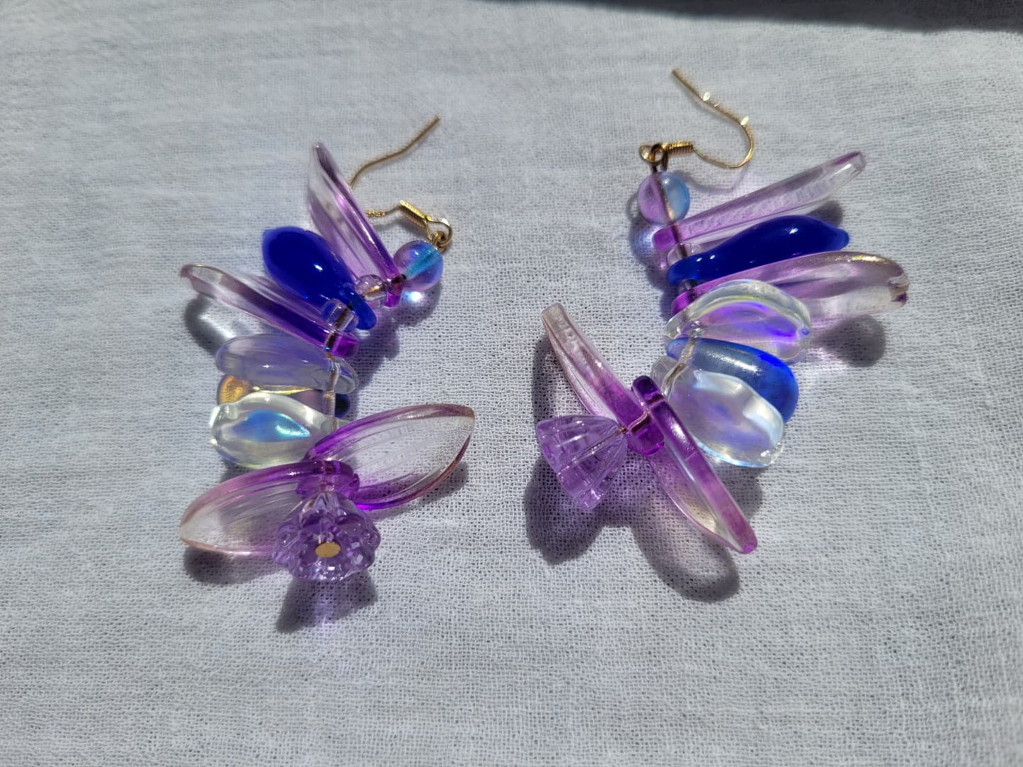 Colorful petal-shaped earrings with purple, blue and white glass beads on a light gray fabric background