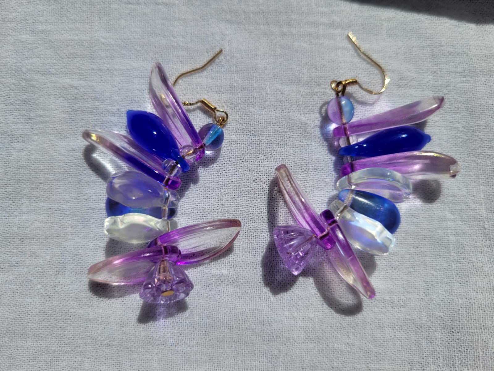 Colorful petal-shaped earrings with purple, blue and white glass beads on a light gray fabric background