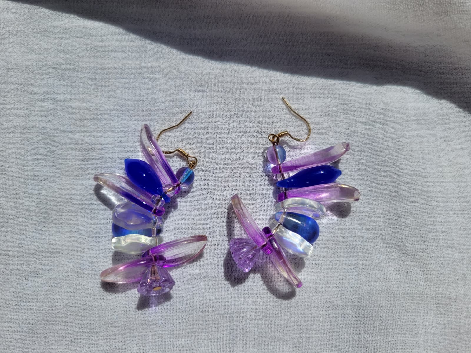 Colorful petal-shaped earrings with purple, blue and white glass beads on a light gray fabric background.