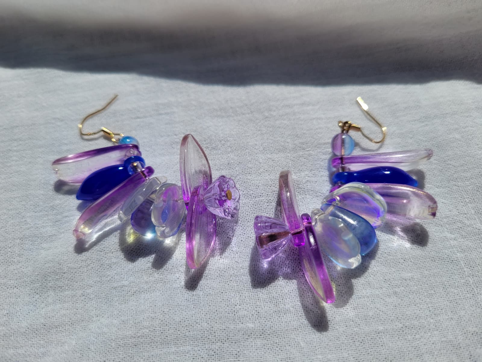 Colorful petal-shaped earrings with purple, blue and white glass beads on a light gray fabric background