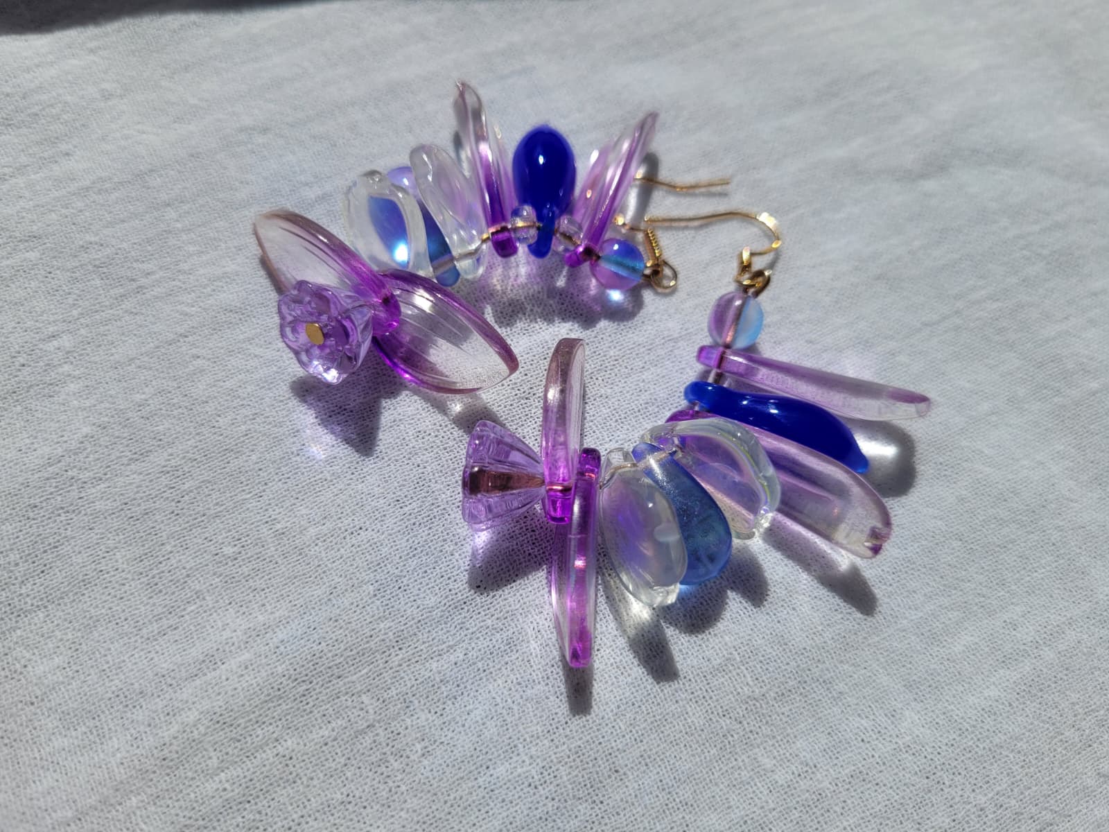 Colorful petal-shaped earrings with purple, blue and white glass beads on a light gray fabric background