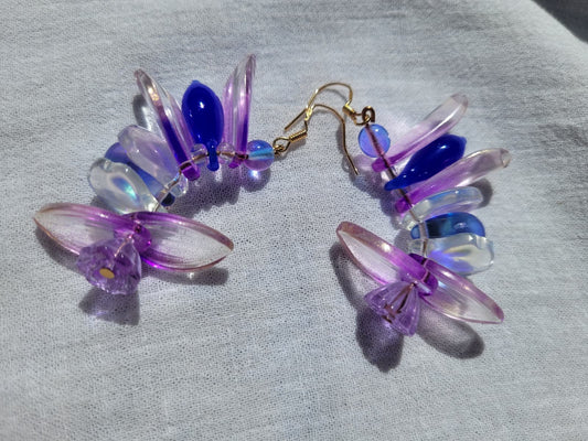 Colorful petal-shaped earrings with purple, blue and white glass beads on a light gray fabric background