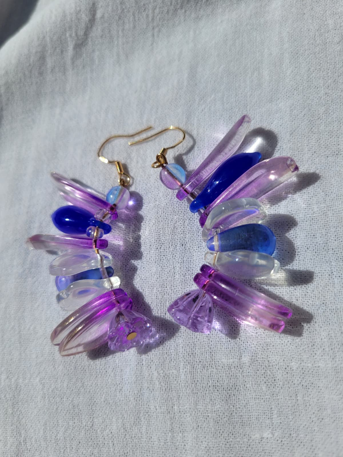 Colorful petal-shaped earrings with purple, blue and white glass beads on a light gray fabric background