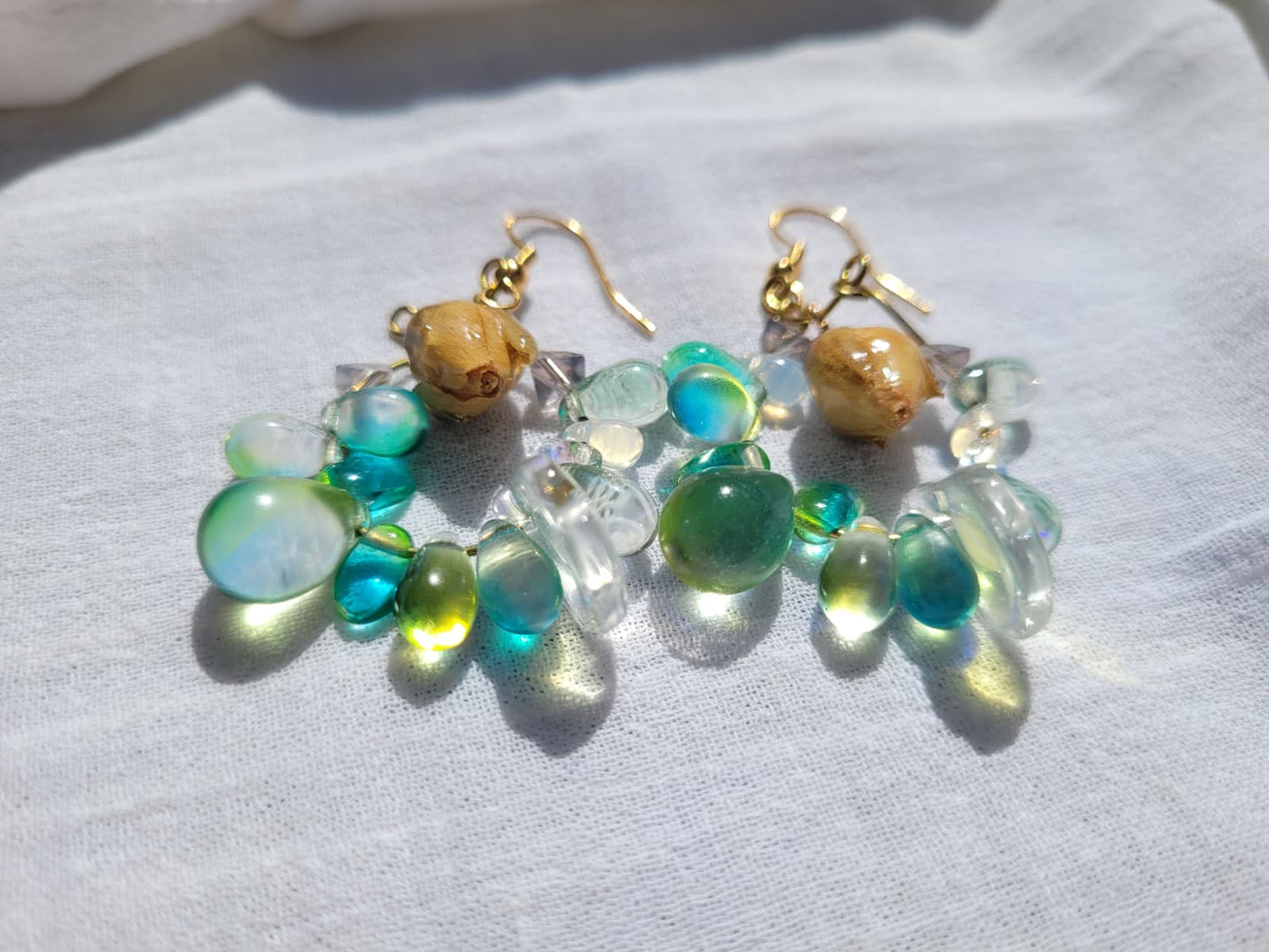 Pair of earrings with green and gold beads, natural dried yellow rose buds, gold-plated hooks on a light gray background