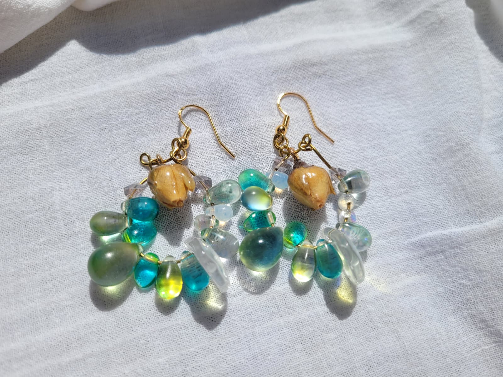 Pair of earrings with green and turquoise beads, natural dried yellow rose buds, gold-plated hooks on a light gray background