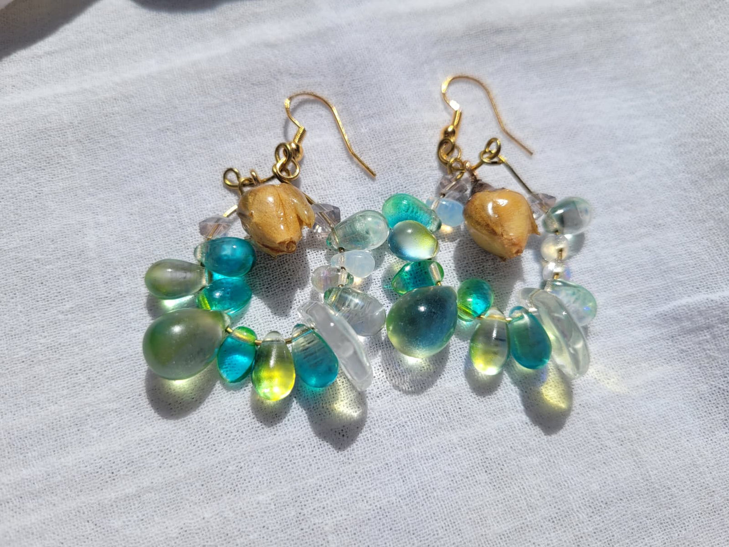 Pair of earrings with green and gold beads, natural dried yellow rose buds, gold-plated hooks on a light gray background