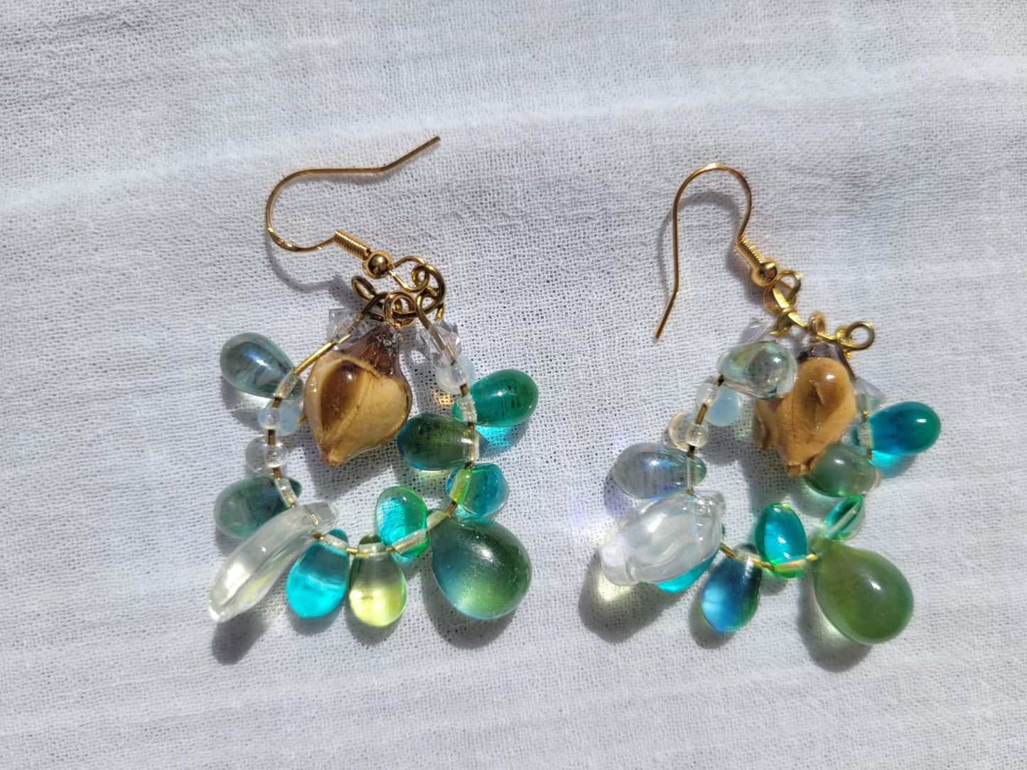 Pair of earrings with green and turquoise beads, natural dried yellow rose buds, gold-plated hooks on a light gray background