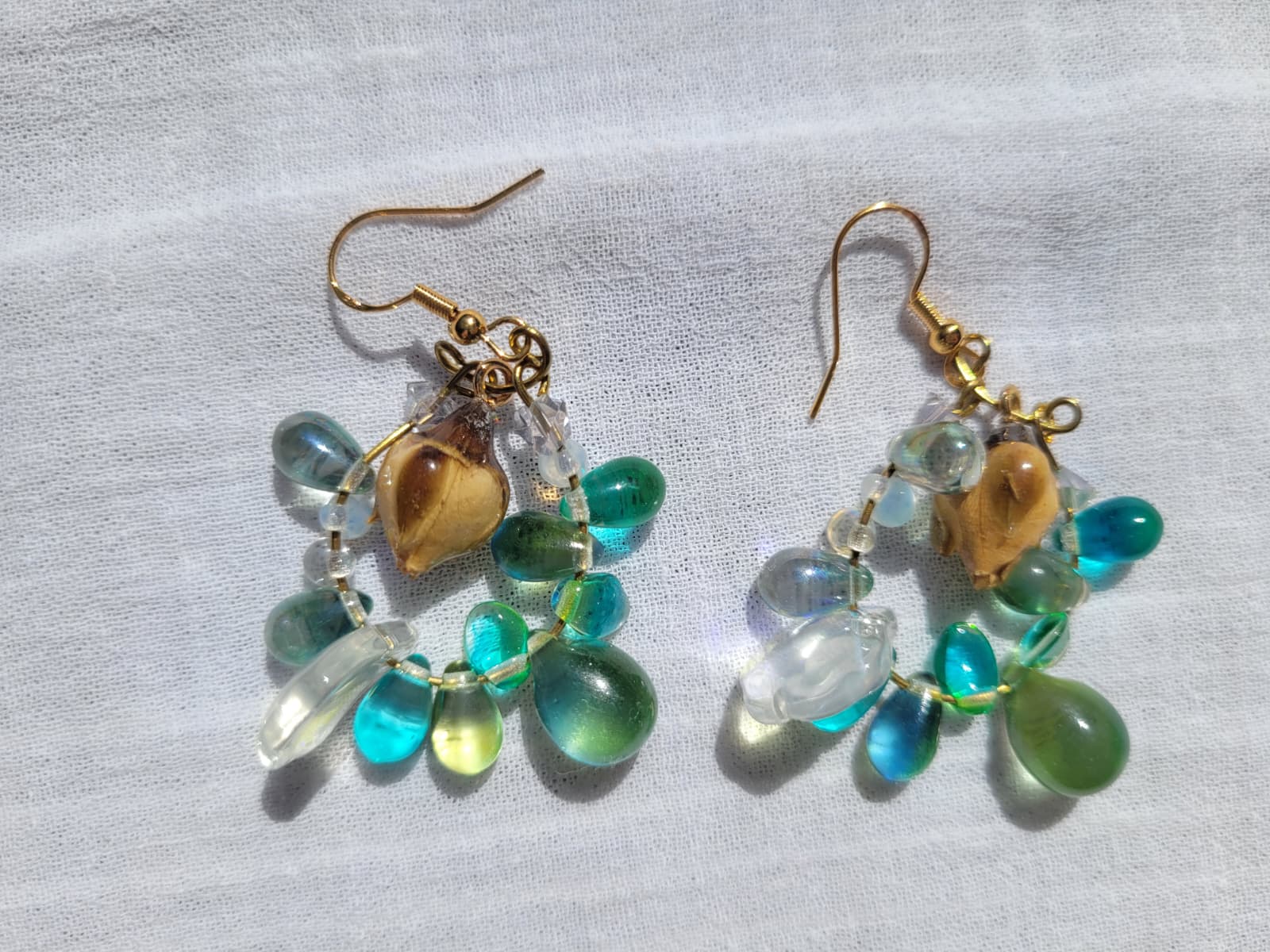Pair of earrings with green and turquoise beads, natural dried yellow rose buds, gold-plated hooks on a light gray background