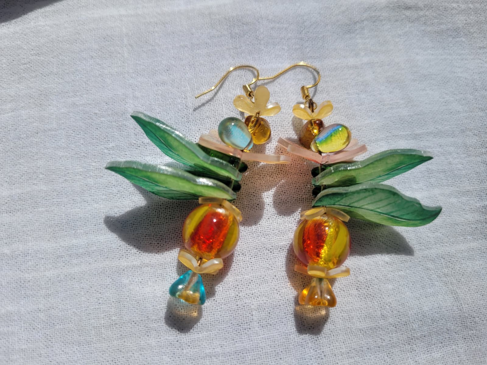 Pair of colorful glass earrings with leaf and flower design, glass czech beads and butterflies on a light gray background
