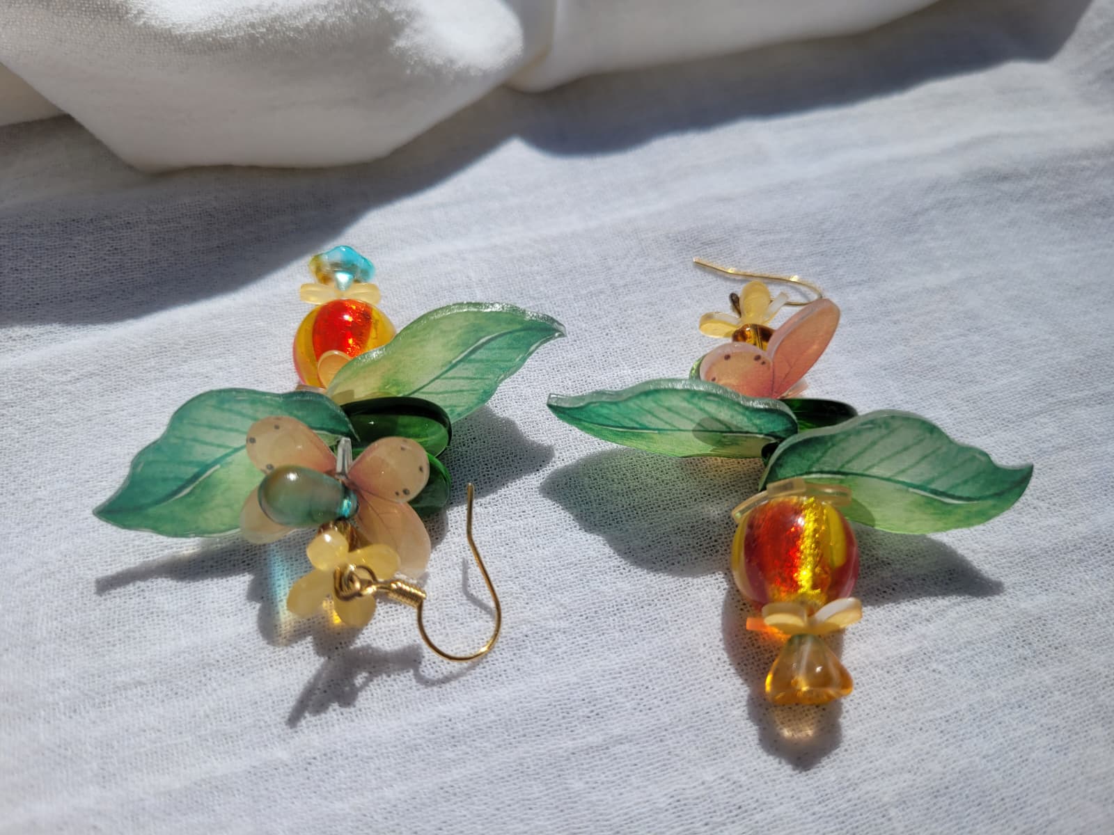 Pair of colorful glass earrings with leaf and flower design, glass czech beads and butterflies on a light gray background